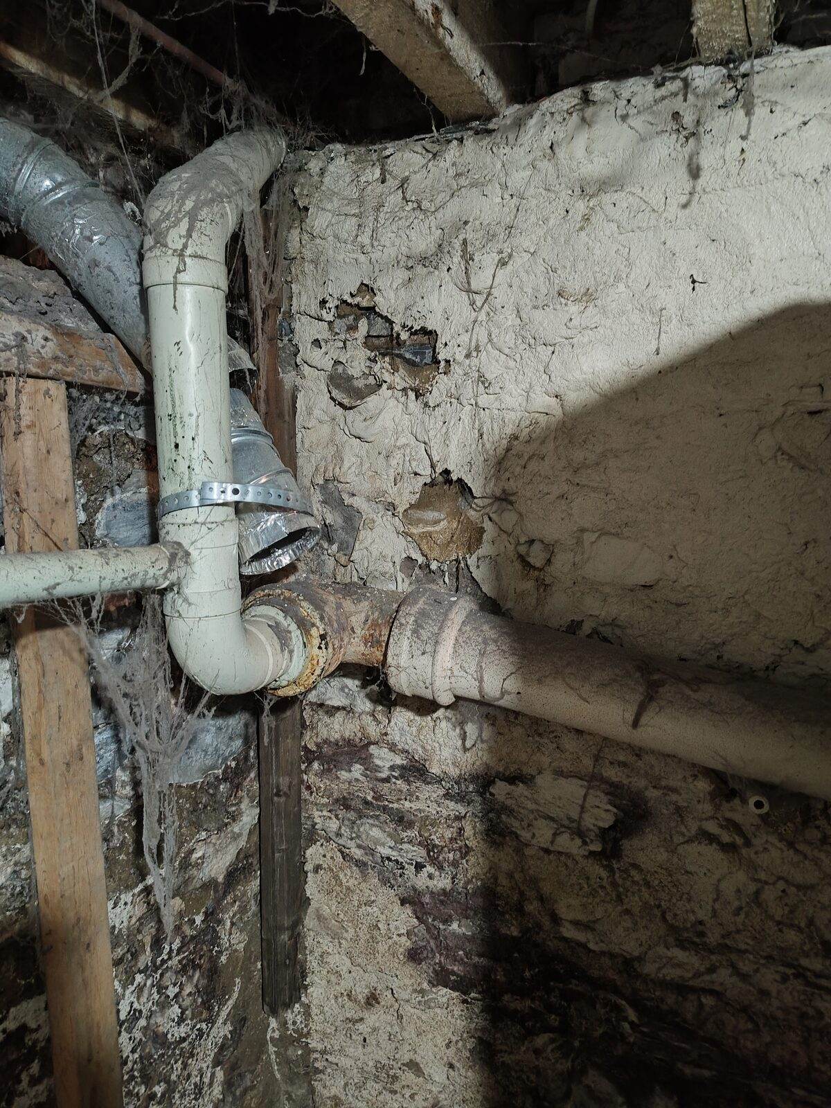 Old cast-iron drain piping running through the stone foundation wall of an older Lancaster County basement.