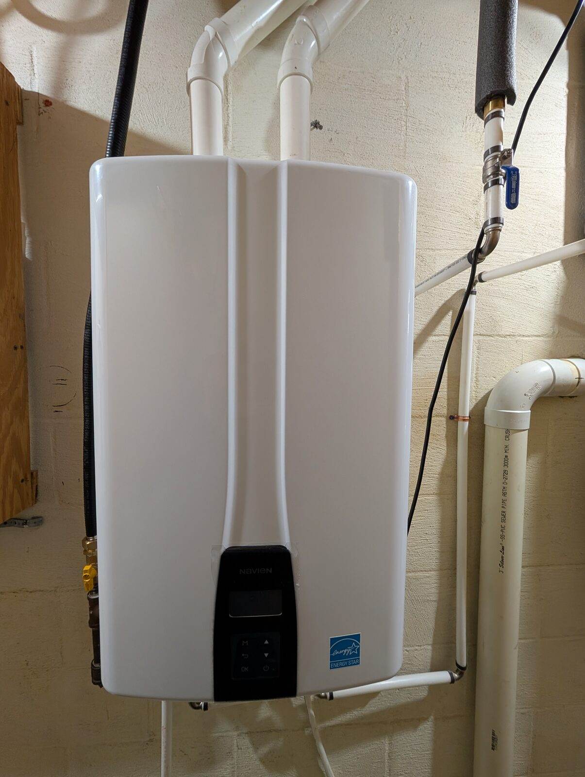 A wall-mounted tankless water heater installed by Tom Falk, with new water and gas connections in a basement.