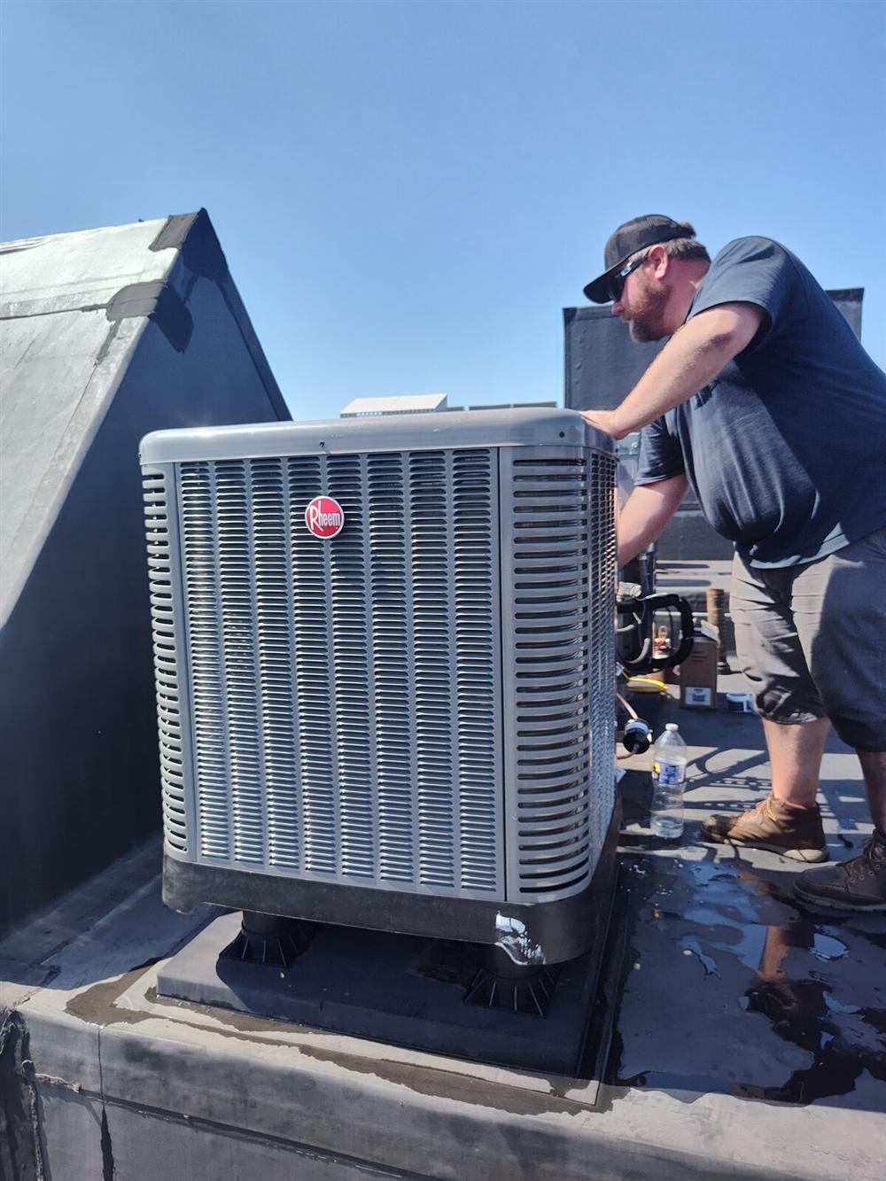 Tom Falk technician Jim installing a Rheem AC condenser on a Lancaster rooftop.